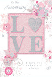 This anniversary card is presented in a close, detailed view, revealing a gentle celebration of enduring romance in soft pastel pinks and silvery greys, much like the calm atmosphere of an early evening stroll through Waterloo. At the centre, the word LOVE appears in raised, softly sparkling glitter, giving each letter a plush, tactile surface. The O is replaced by a shimmering heart motif in textured silver, standing out like a jewel amid the blush-toned background. Surrounding this focal word, delicate blooms in blush and mauve unfurl in an almost watercolour style, their edges softened and slightly translucent, as if lightly washed onto the card. Fine curling vines, tiny petals, and faint butterflies weave around the flowers, adding a sense of graceful movement, like petals drifting down along Waterloo's quieter back streets. The card's base colour stays within a muted pink and cream spectrum, allowing the silver highlights and glitter details to glint softly rather than dazzle. Across the design, elegant script phrases such as On Our Anniversary and I love you today and always are written in a flowing, understated font that feels personal, like a handwritten note slipped between bouquet stems. The overall impression is of a thoughtful keepsake, tender and refined, echoing the care a Waterloo florist puts into crafting anniversary arrangements for delivery across the SE1 area. With its layered textures, romantic heart detail, and painterly flowers, the card looks ready to accompany a beautifully arranged anniversary bouquet, quietly marking another cherished year together.